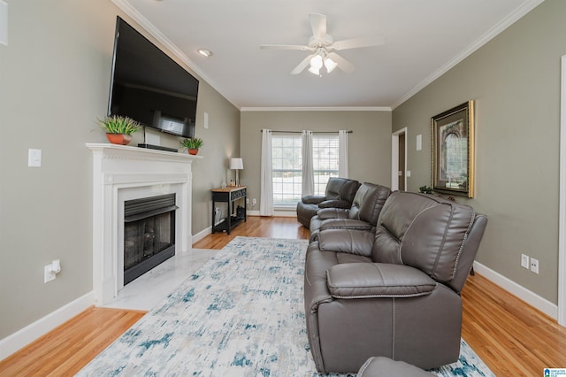living area with baseboards, a ceiling fan, wood finished floors, crown molding, and a high end fireplace