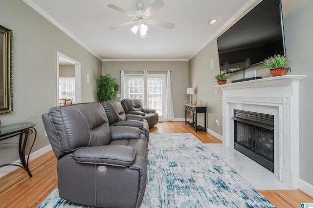 living room with baseboards, a premium fireplace, wood finished floors, ceiling fan, and ornamental molding