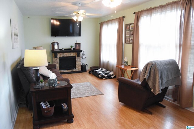 living room featuring ceiling fan, wood-type flooring, and a stone fireplace