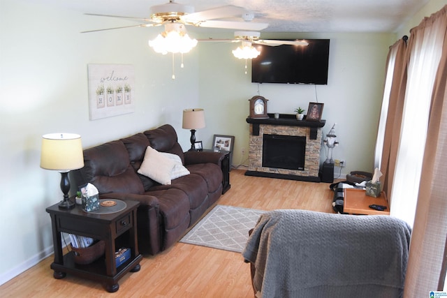 living room with ceiling fan, light hardwood / wood-style floors, and a stone fireplace