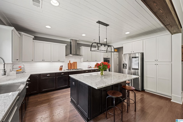 kitchen with dark hardwood / wood-style flooring, wall chimney range hood, a kitchen island, and appliances with stainless steel finishes