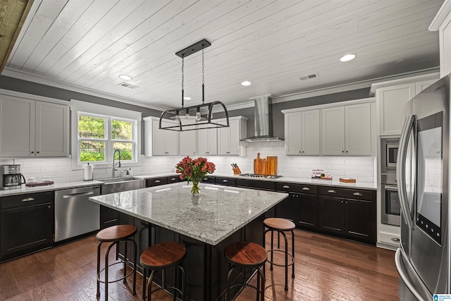 kitchen with stainless steel appliances, decorative light fixtures, a kitchen island, wall chimney range hood, and dark hardwood / wood-style flooring