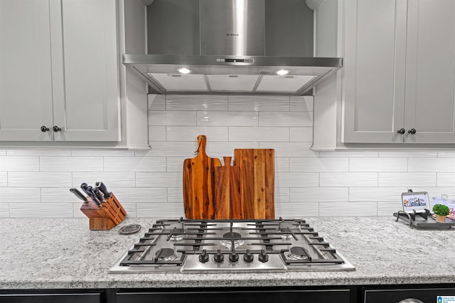 kitchen featuring decorative backsplash, wall chimney exhaust hood, stainless steel gas stovetop, and light stone counters