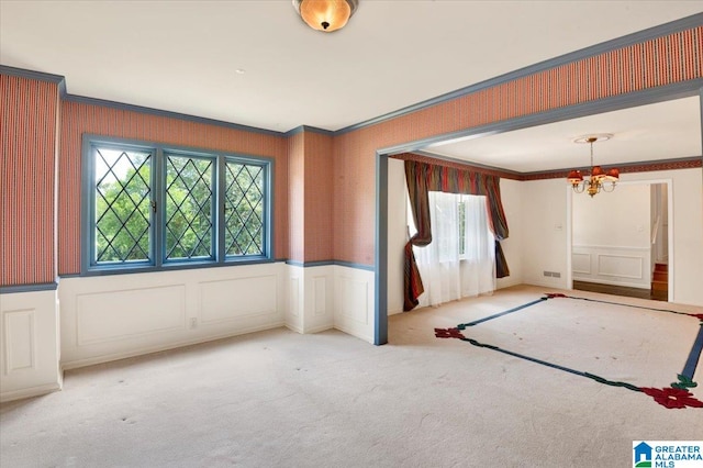 carpeted spare room featuring crown molding, plenty of natural light, and a chandelier