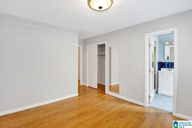 unfurnished bedroom featuring a closet, light wood-type flooring, and ensuite bathroom