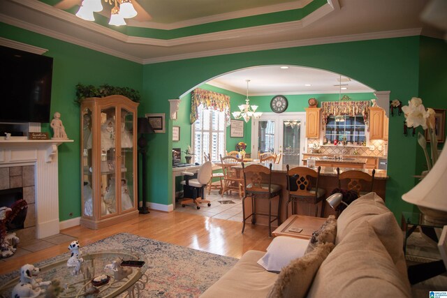 living room featuring ornamental molding, ceiling fan with notable chandelier, light hardwood / wood-style flooring, a tile fireplace, and a raised ceiling