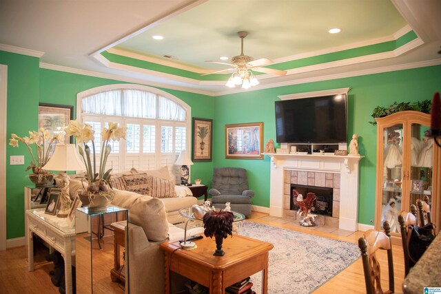 living room featuring a tray ceiling, ceiling fan, a fireplace, and light hardwood / wood-style floors