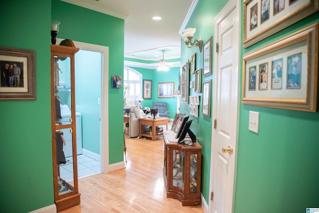 corridor with light hardwood / wood-style flooring, washer / dryer, and ornamental molding