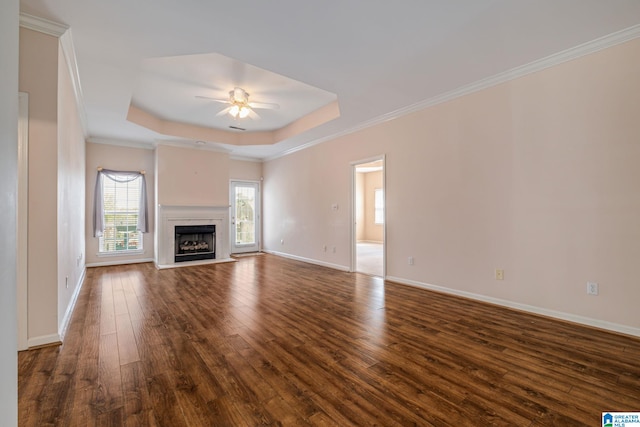 unfurnished living room with crown molding, a premium fireplace, dark wood-type flooring, ceiling fan, and a raised ceiling