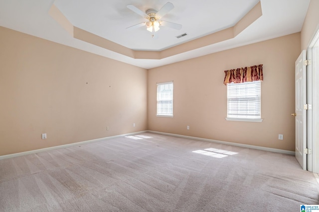 carpeted empty room with plenty of natural light, ceiling fan, and a tray ceiling