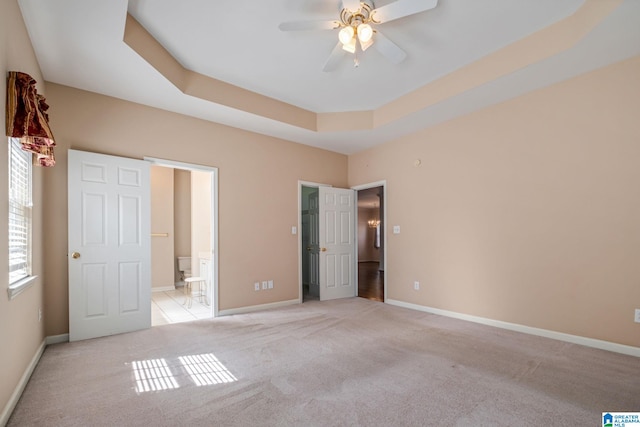 unfurnished bedroom featuring a tray ceiling, light colored carpet, connected bathroom, and ceiling fan