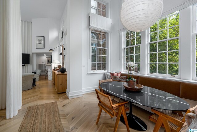 dining space with light parquet flooring, plenty of natural light, and a high ceiling