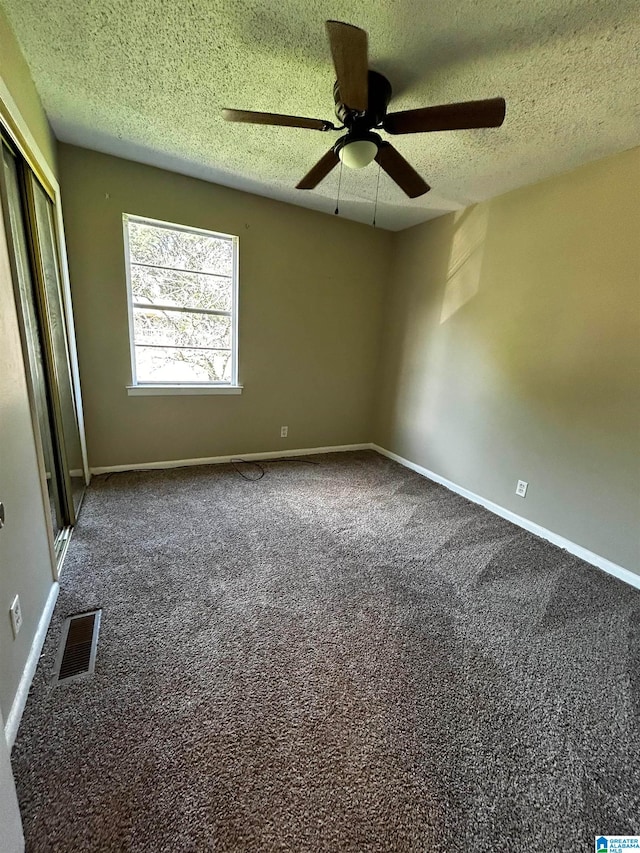 empty room featuring a textured ceiling, carpet floors, visible vents, and baseboards