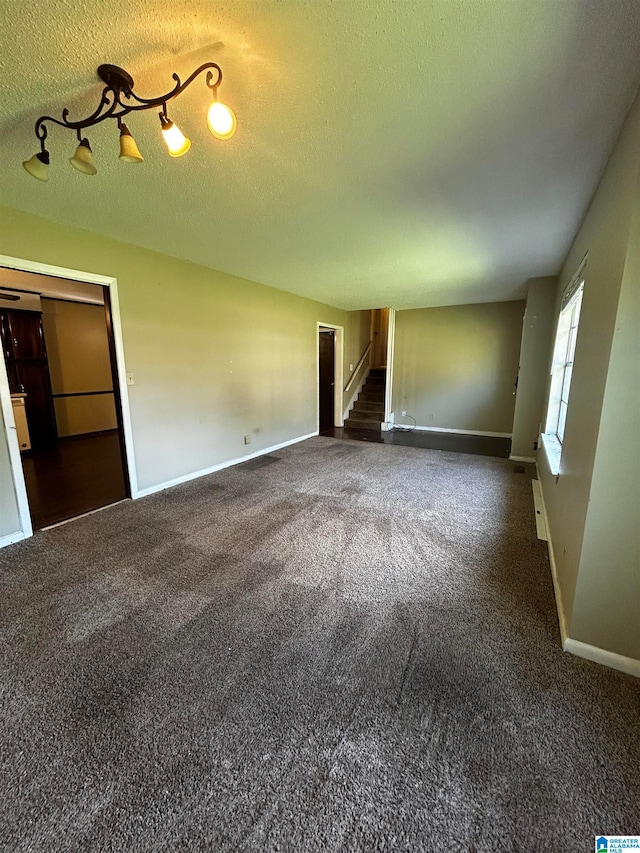 empty room featuring stairs, baseboards, dark colored carpet, and a textured ceiling