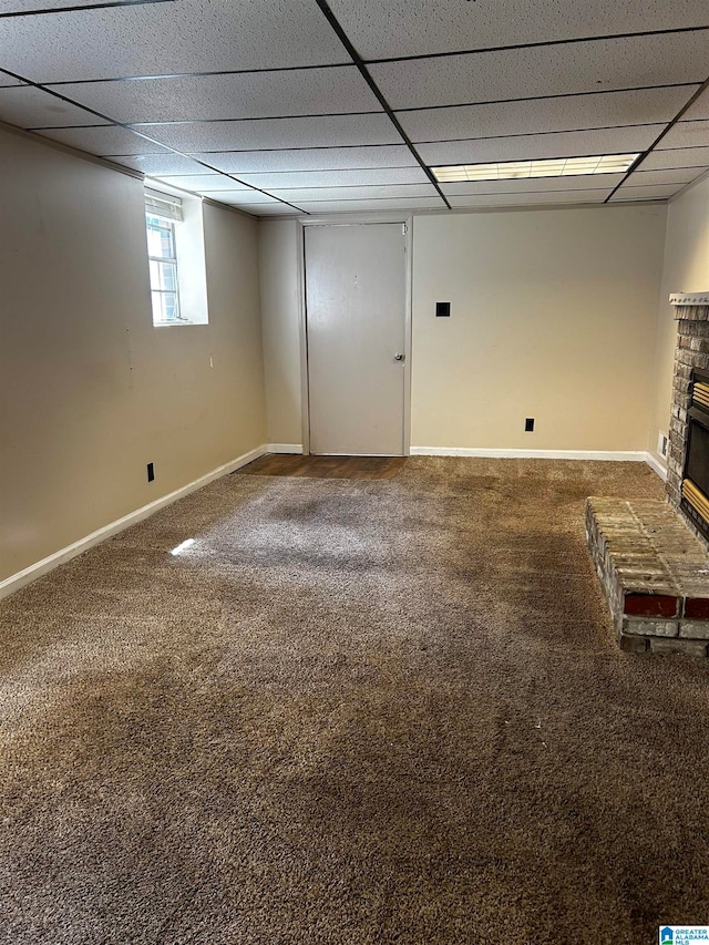 basement featuring baseboards, carpet flooring, a fireplace, and a drop ceiling