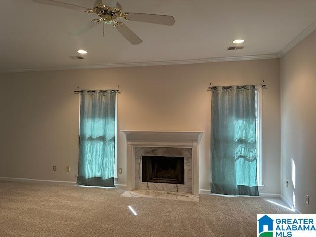 unfurnished living room with ceiling fan, ornamental molding, carpet floors, and a fireplace