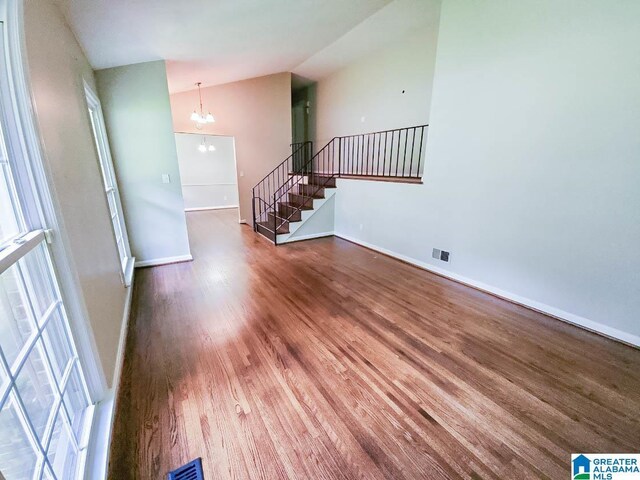 unfurnished living room with vaulted ceiling, a notable chandelier, and hardwood / wood-style flooring