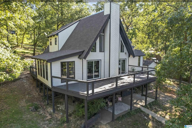 back of property with a shingled roof, a chimney, and a deck