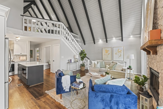 living room with stairway, high vaulted ceiling, beam ceiling, a fireplace, and wood finished floors