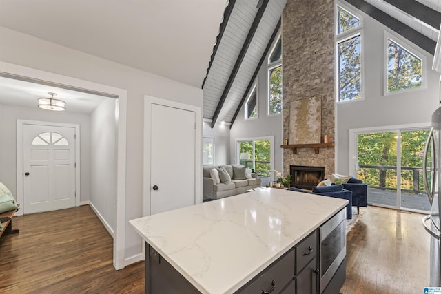 kitchen with a kitchen island, light stone countertops, a stone fireplace, stainless steel microwave, and dark wood-type flooring