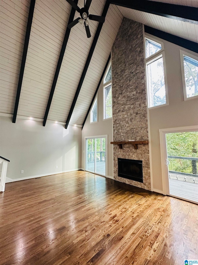 unfurnished living room featuring beamed ceiling, a stone fireplace, wood-type flooring, high vaulted ceiling, and ceiling fan