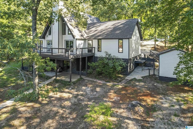 rear view of house featuring a deck, a patio, and roof with shingles