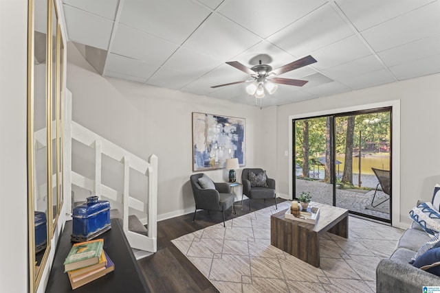 living room with baseboards, wood finished floors, ceiling fan, and a paneled ceiling
