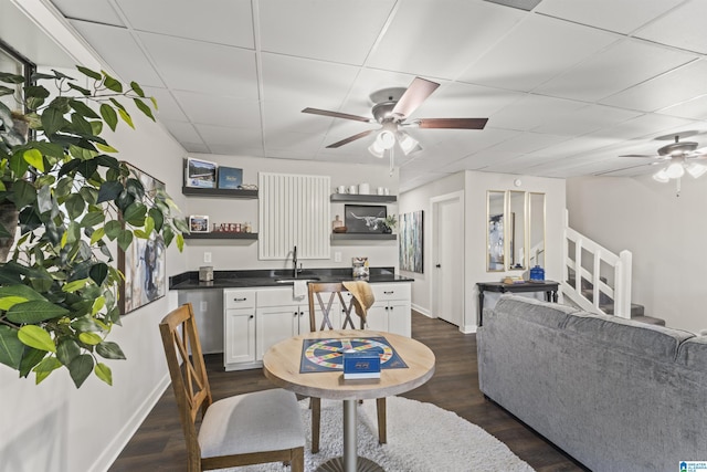 dining room featuring baseboards, a drop ceiling, dark wood-type flooring, and a ceiling fan