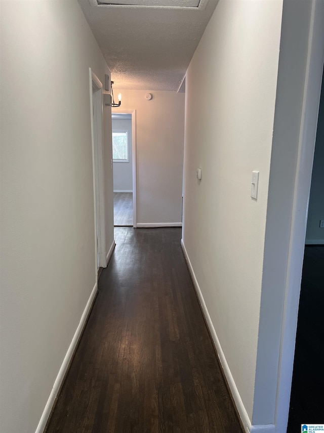 hallway featuring dark wood-style floors, baseboards, and a textured ceiling