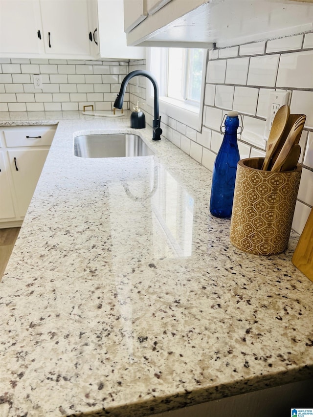 room details with white cabinets, light stone countertops, decorative backsplash, and a sink