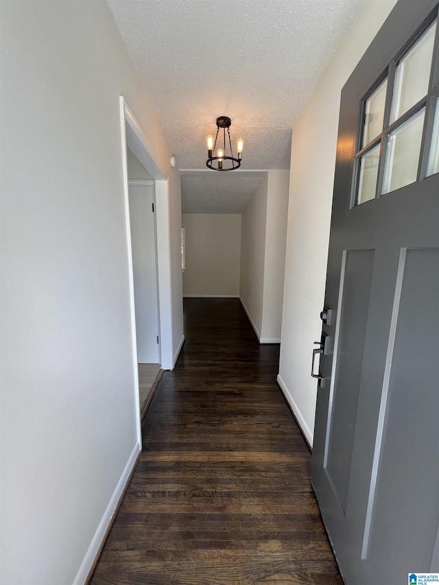 hallway featuring a chandelier, a textured ceiling, baseboards, and dark wood-style floors