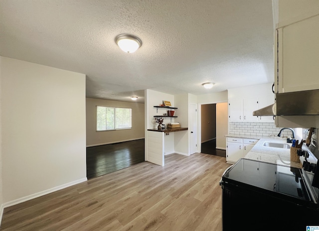 kitchen with black electric range, backsplash, light wood-style floors, white cabinetry, and a sink