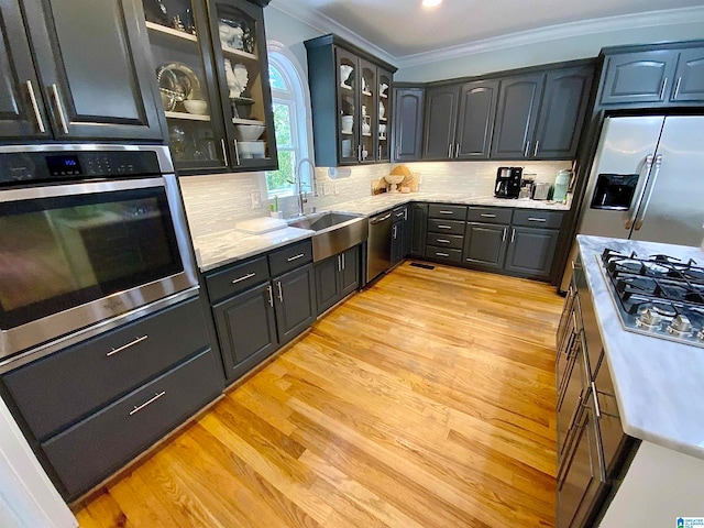 kitchen with backsplash, crown molding, light wood-type flooring, appliances with stainless steel finishes, and sink