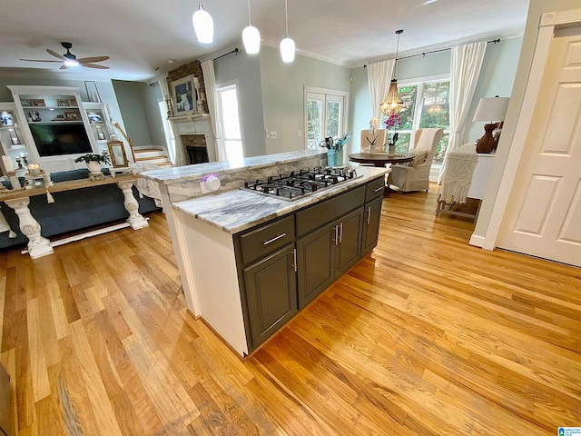 kitchen with a large fireplace, hanging light fixtures, light hardwood / wood-style flooring, light stone countertops, and ceiling fan