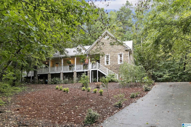 view of front of property with a porch, stone siding, stairway, and a view of trees