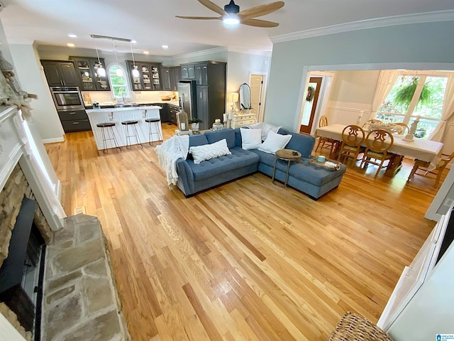 living room featuring ceiling fan, ornamental molding, light wood-type flooring, and a fireplace