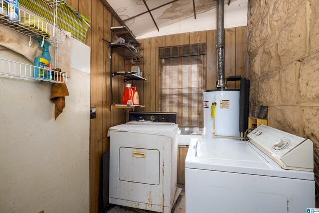 clothes washing area with wood walls, independent washer and dryer, and water heater