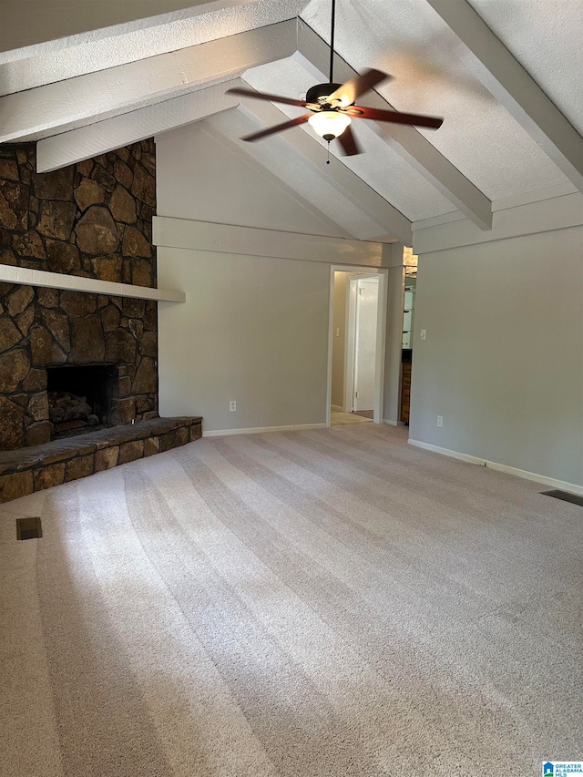 unfurnished living room with carpet flooring, ceiling fan, a stone fireplace, lofted ceiling with beams, and a textured ceiling