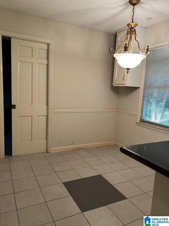 unfurnished dining area with light tile patterned floors, baseboards, and a textured ceiling