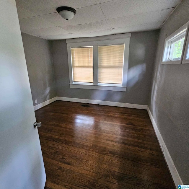 spare room with a paneled ceiling and dark hardwood / wood-style flooring