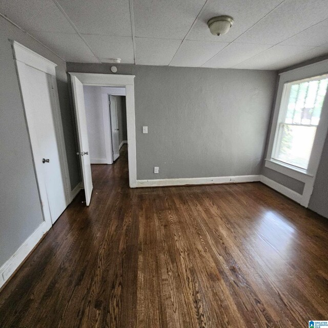 empty room with a drop ceiling and dark wood-type flooring