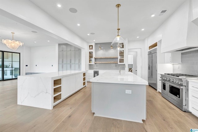 kitchen with high end appliances, a large island with sink, light stone counters, and decorative backsplash