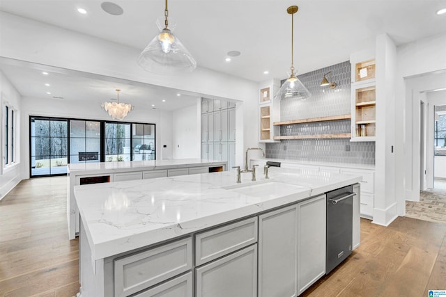 kitchen with light wood-type flooring, light stone counters, decorative light fixtures, and an island with sink