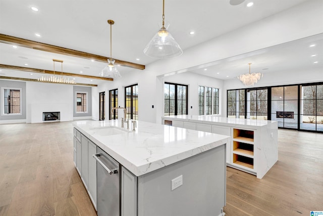 kitchen featuring stainless steel dishwasher, light wood-type flooring, an island with sink, and sink