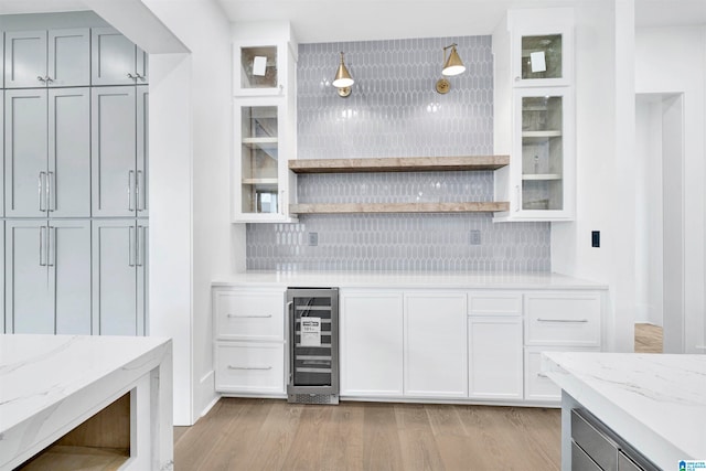 bar featuring light wood-type flooring, wine cooler, light stone countertops, and decorative backsplash