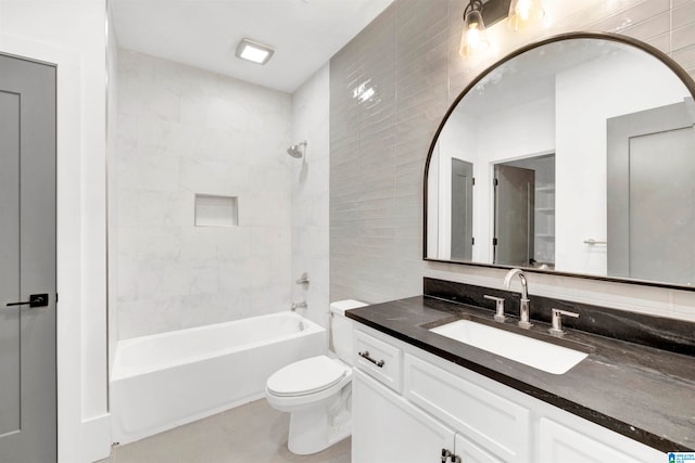 full bathroom with tile walls, tiled shower / bath, toilet, and vanity