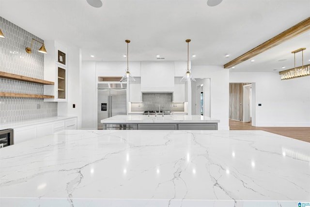 kitchen featuring an island with sink, built in fridge, decorative backsplash, and white cabinetry