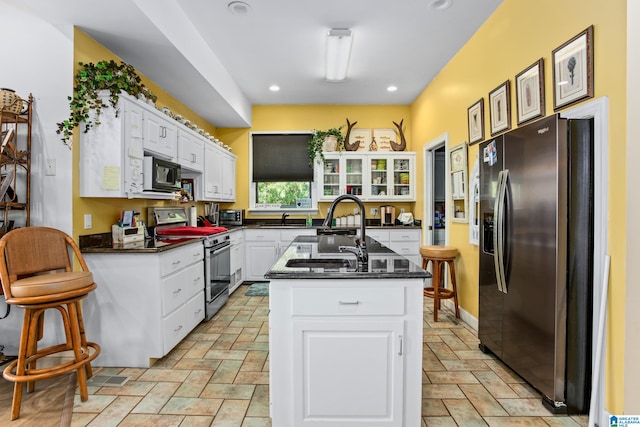 kitchen with sink, an island with sink, appliances with stainless steel finishes, white cabinetry, and a breakfast bar area