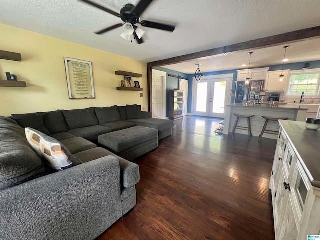 living room featuring beamed ceiling, a textured ceiling, dark hardwood / wood-style flooring, ceiling fan, and french doors