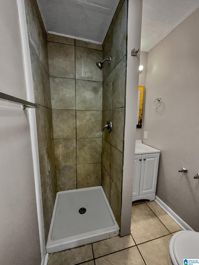 bathroom with a textured ceiling, vanity, tiled shower, tile patterned flooring, and toilet